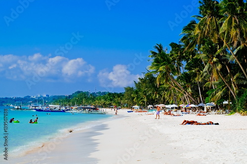 Beautiful tropical white sand beach with coconut palms and people on the beach © Ivan Trizlic