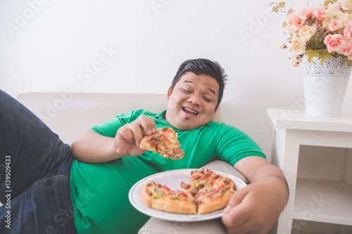 lazy overweight man eating pizza while laying on a couch