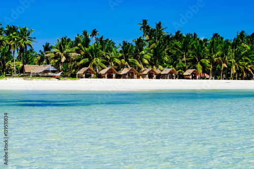 Beautiful white coral sand beach with palms and cottages  turquoise blue ocean