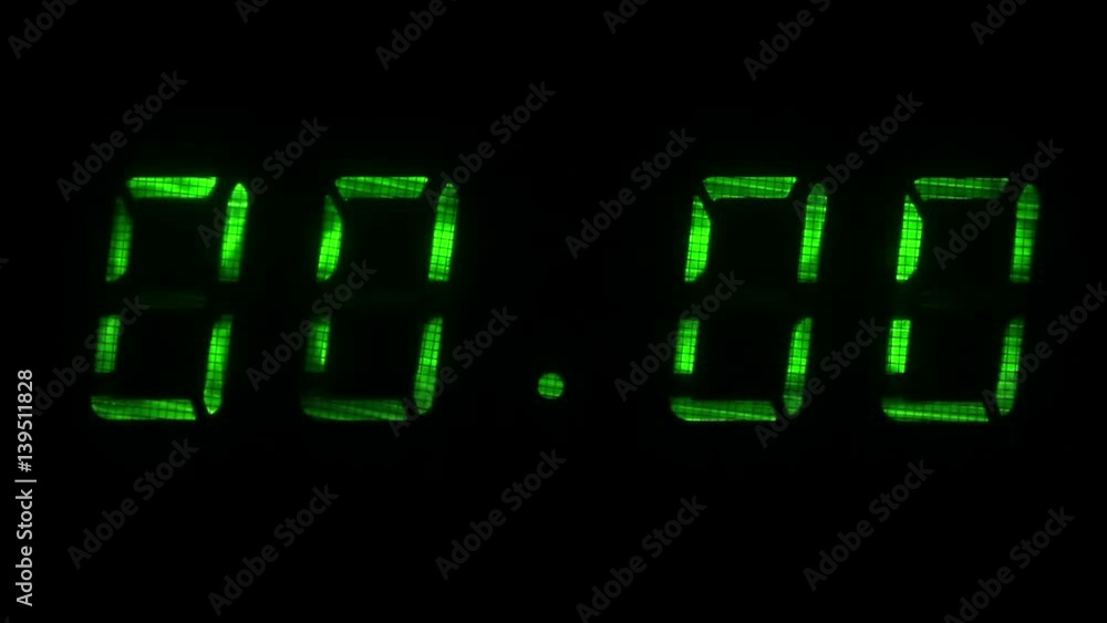 Digital clock with fluorescent display shows the time of 23 hours 59 minutes to 00 hours 00 minutes in the green on a black background Digital clock with fluorescent display shows the time of 23 hours 59 minutes to 00 hours 00 minutes in the green on a black background