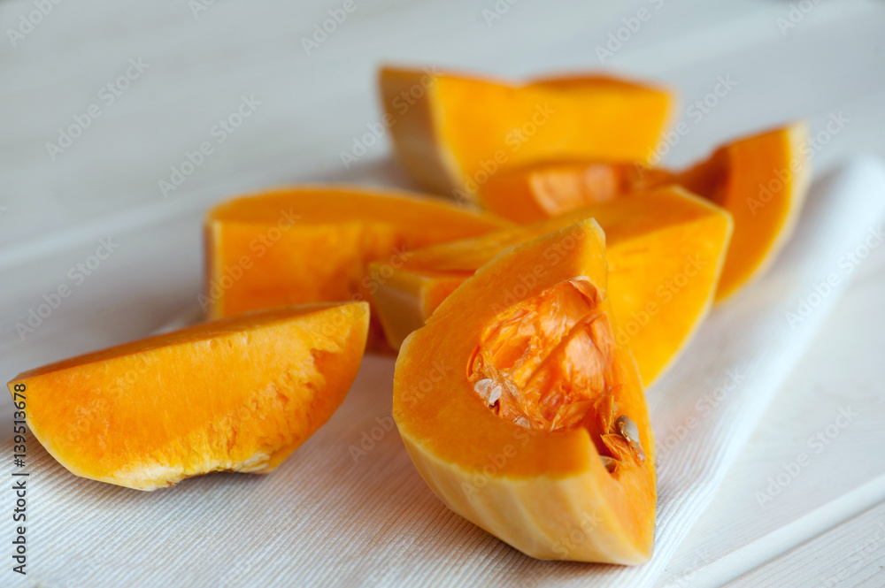 Raw orange pumpkin pieces on the background of textile and wood
