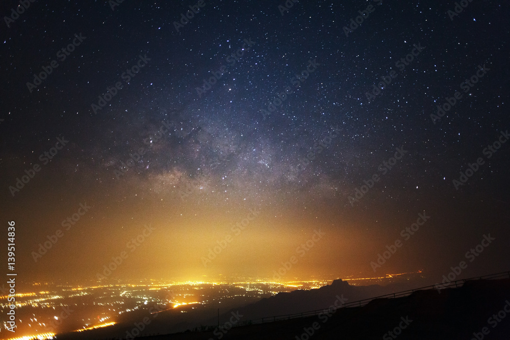 Naklejka premium Milky way galaxy and city light at Phutabberk Phetchabun in Thailand.Long exposure photograph.With grain
