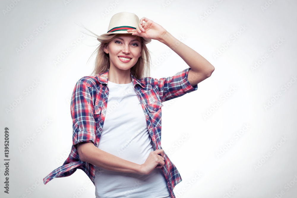 Closeup fashion studio portrait of hipster young smiling woman in white hat and plaid shirt over light blue background Closeup fashion studio portrait of hipster young smiling woman in white hat and plaid shirt over light blue background