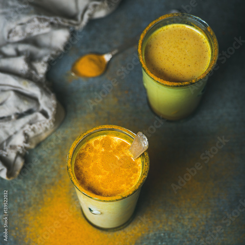 Golden milk with turmeric powder in glasses over dark grunge background, square crop, copy space. Health and energy boosting, flu remedy, natural cold fighting drink. Clean eating, weight loss concept