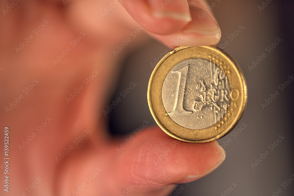 Macro of one euro coin between female fingers Macro of one euro coin between female fingers