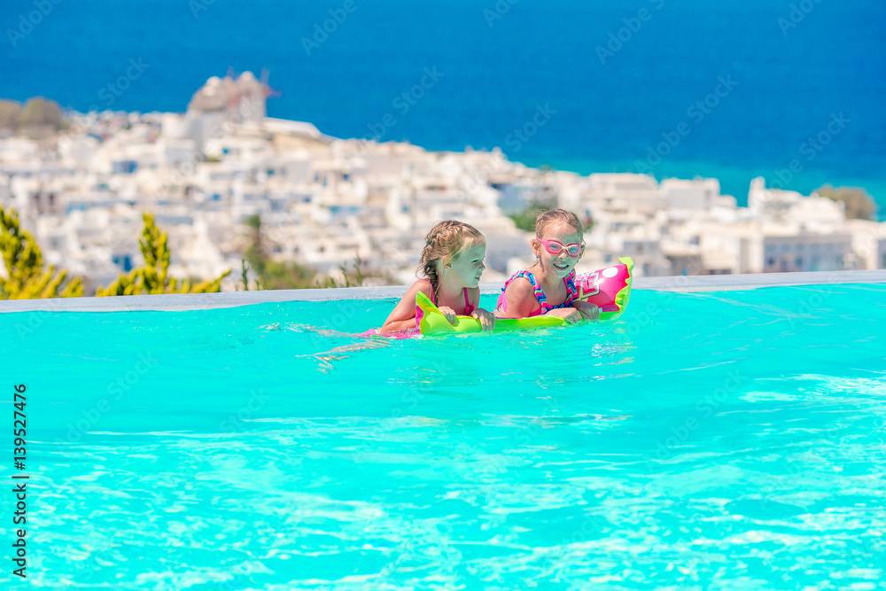 Adorable little girls playing in outdoor swimming pool with beautiful view