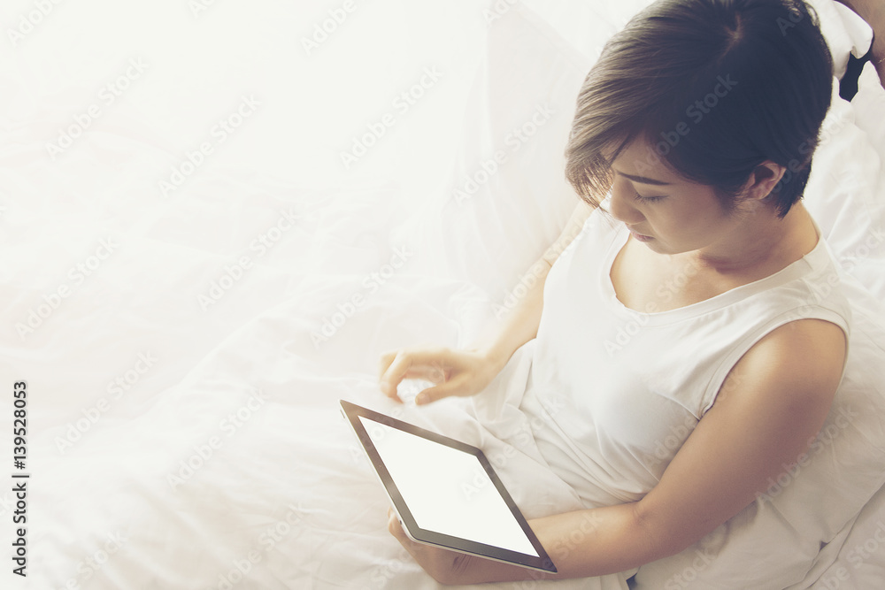 Beautiful Asian women wear white shirt and play a tablet sit on a bed. Beautiful Asian women wear white shirt and play a tablet sit on a bed.
