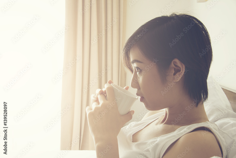 Beautiful Asian women wear white shirt hold a coffee or tea cup and sit on a bed. Beautiful Asian women wear white shirt hold a coffee or tea cup and sit on a bed.