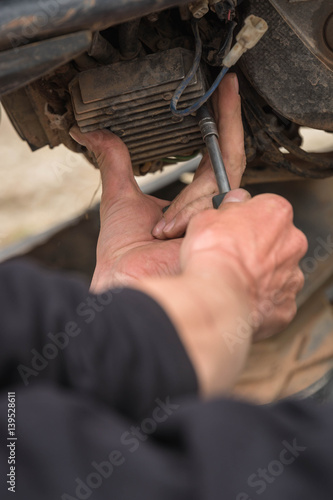 Man repairing on a motorcycle. Man under motorcycle working on the gas pump. © skinfaxi