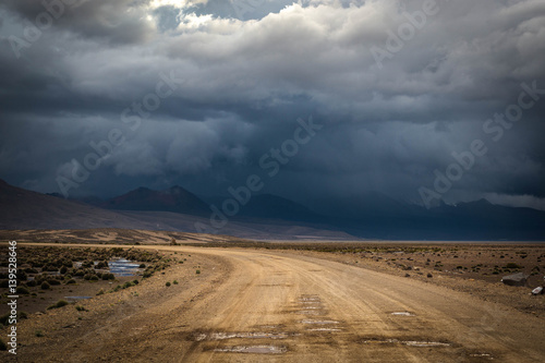 Landscape with dirt road in the mountains under stormy sky.Rural mountain road in Peru, South America, just before the snow storm. Mountains in the background. © skinfaxi