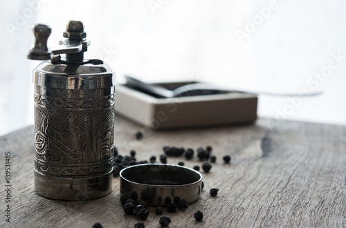 Old pepper mill and peppercorns on wooden board