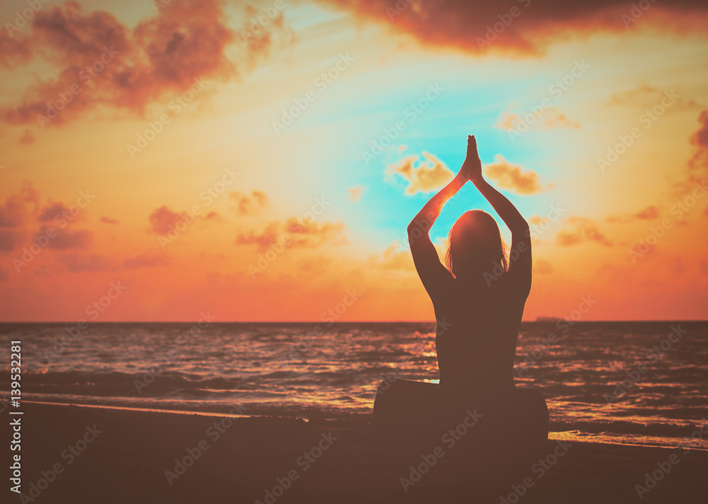 young woman doing yoga on sunset beach