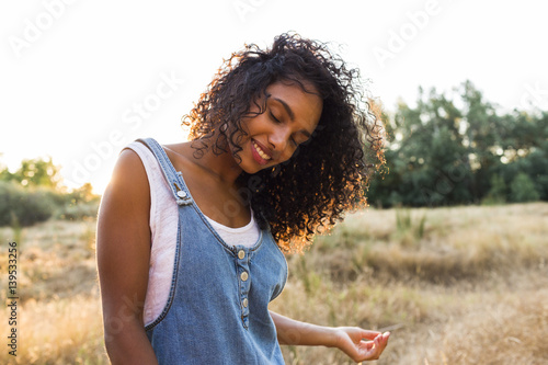 portrait outdoors of a beautiful young afro american woman smiling at sunset. Yellow background. Lifestyle