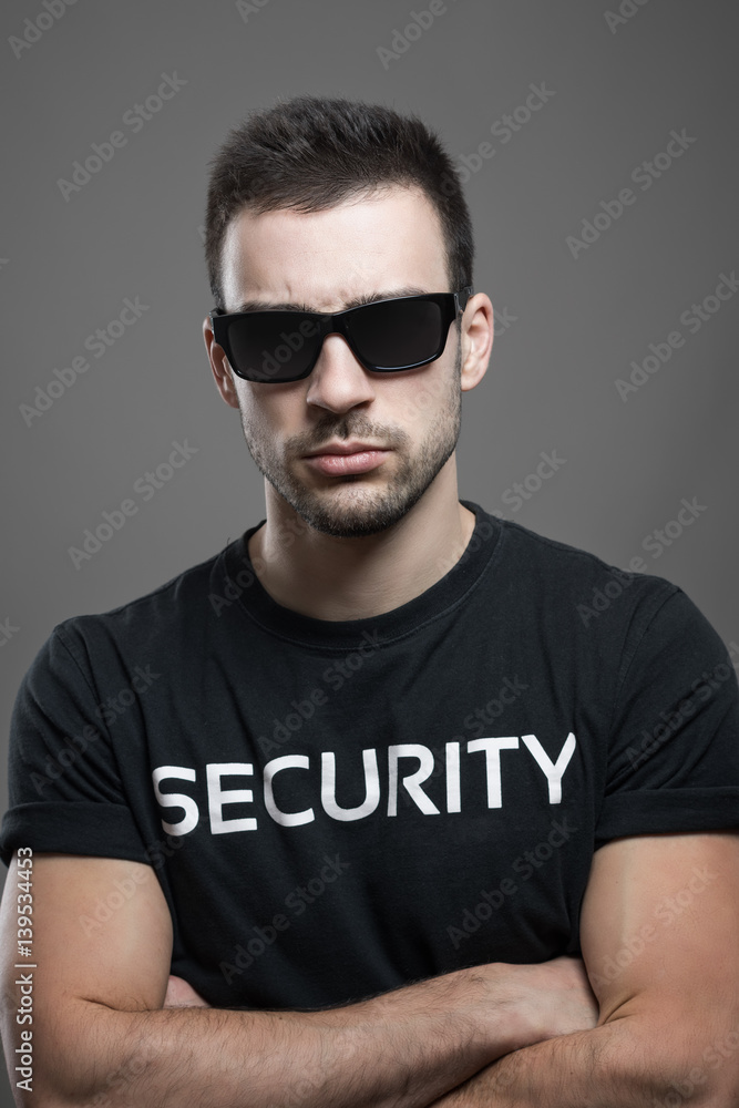 Tough macho serious male security guard with sunglasses and crossed arms looking at camera over dark gray studio background. Tough macho serious male security guard with sunglasses and crossed arms looking at camera over dark gray studio background.