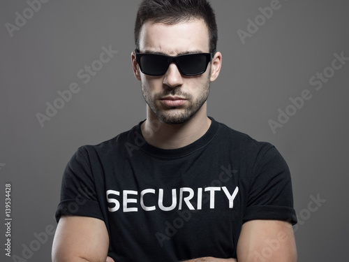 Cuadro en lienzo Dramatic portrait of tough macho security guard man with crossed arms over dark gray studio background