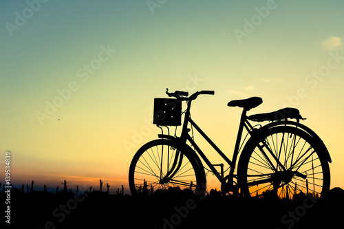 Silhouette of old bicycle on grass with the sky sunset, color of vintage tone and soft focus concept journey