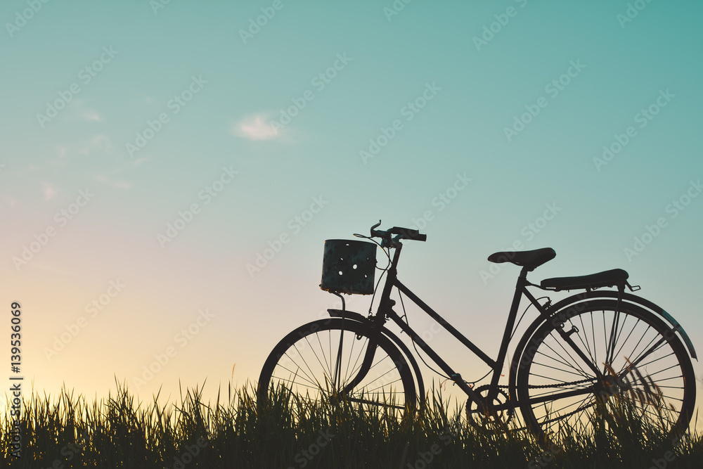Silhouette of old bicycle on grass with the sky sunset, color of vintage tone and soft focus concept journey