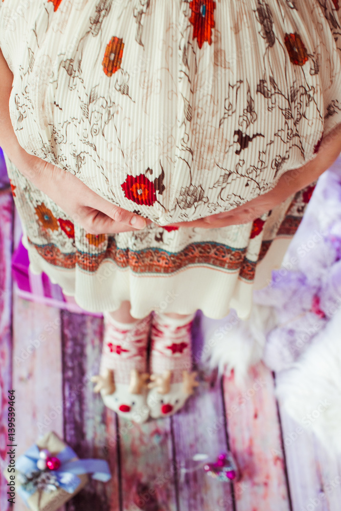Woman in dress with red flowers holds her pregnant belly