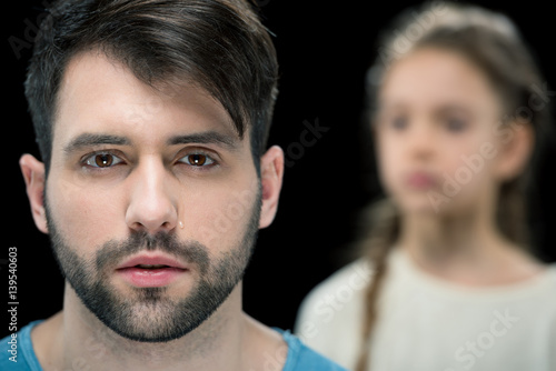 portrait of bearded man with little girl behind on black