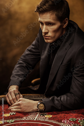 Serious handsome man in suit sitting at poker table and looking away