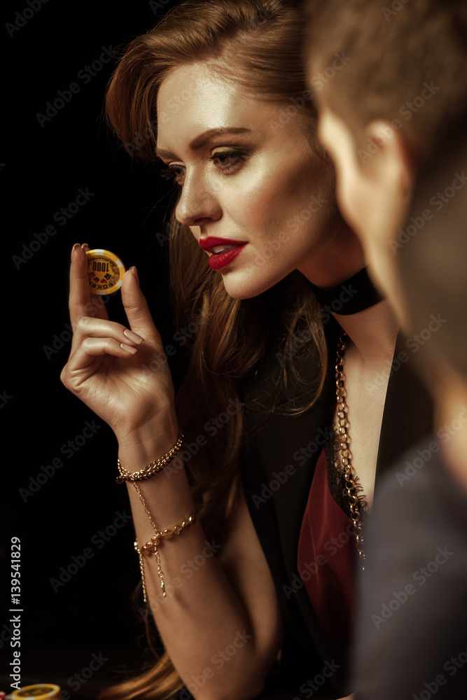 Beautiful young woman in evening dress holding casino chip on black