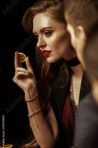 Beautiful young woman in evening dress holding casino chip on black