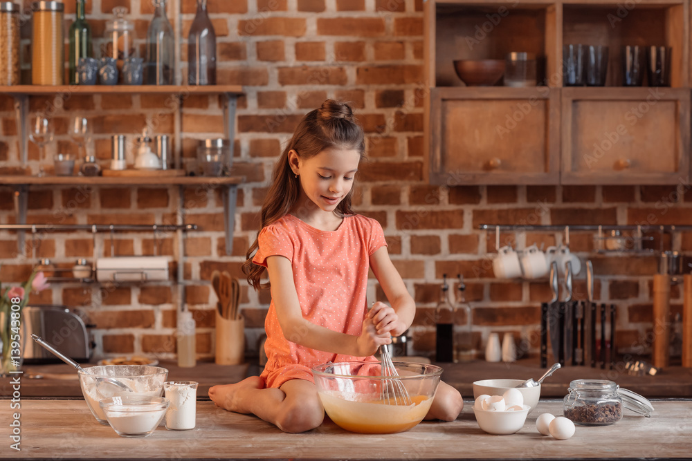 'Girl sitting on table and mixing ingredients for dough for cake 'Girl sitting on table and mixing ingredients for dough for cake