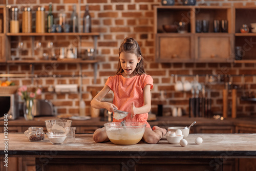  girl sitting on table and mixing ingredients for dough for cake