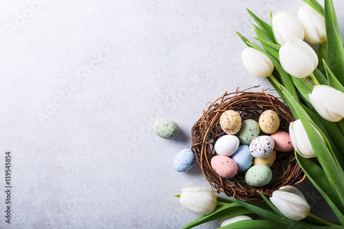 Beautiful white tulips with colorful quail eegs in nest on light gray stone background. Spring and Easter holiday concept with copy space. #139545854