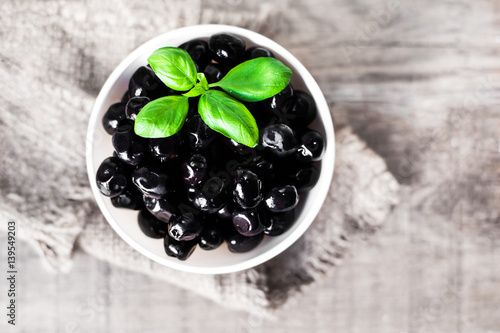 Black olives in a white bowl on wooden table with copy space