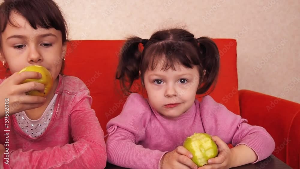 Children eating apples. Two sisters eating yellow apples while sitting on an orange couch. Two little girls indulge. Children eating apples. Two sisters eating yellow apples while sitting on an orange couch. Two little girls indulge.
