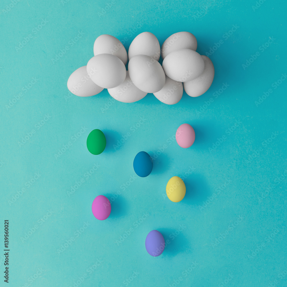 Fototapeta premium Cloud and rain made of colorful easter eggs on blue background. Flat lay. Minimal concept.
