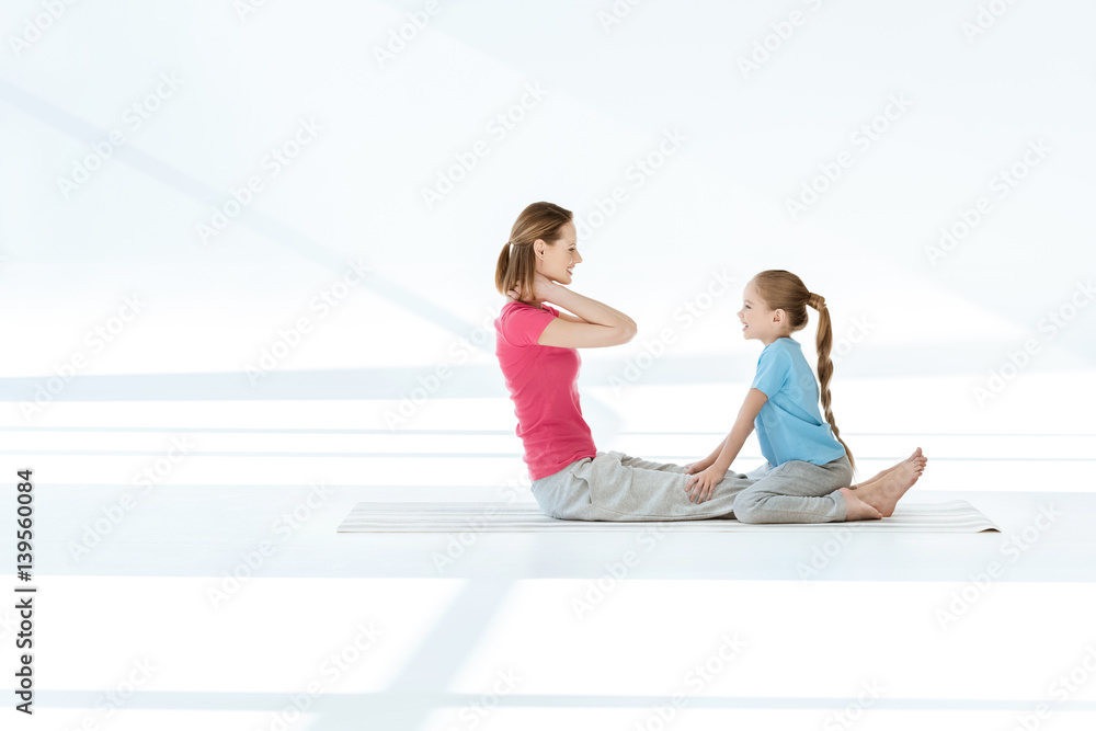 Side view of smiling daughter training happy mother on yoga mat