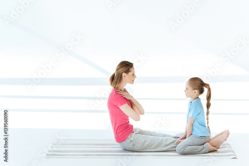 Side view of smiling daughter training happy mother on yoga mat