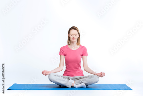 Sporty woman practicing lotus yoga position on mat on white