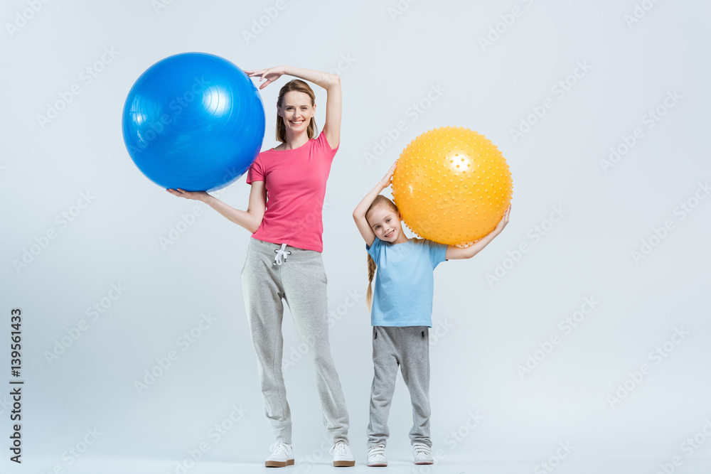 smiling mother and daughter holding fitness balls on white smiling mother and daughter holding fitness balls on white