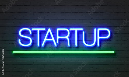 Startup neon sign on brick wall background.