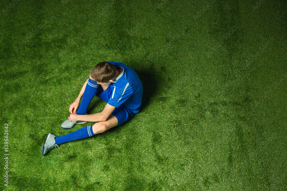 Boy soccer player sitting on green grass
