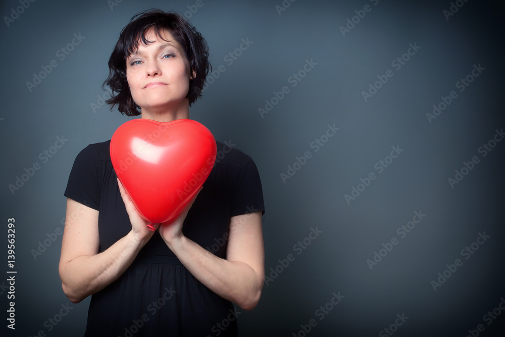 Confident Woman, holding a Red Heart Balloon, on Grey Background with Copy Space Confident Woman, holding a Red Heart Balloon, on Grey Background with Copy Space