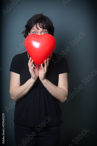 Woman holding a heart Balloon on a Grey Background, playing Peekaboo
