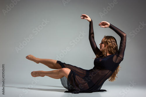 Slika na platnu Young beautiful dancer in black dress posing on a dark gray studio background