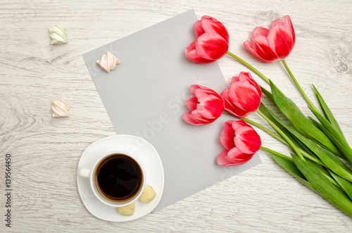 Pink tulips on a blank sheet of paper  mug of coffee and marshmallows  light wooden background. top view  space for text