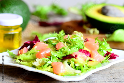Mixed green salad with smoked salmon and avocado and dressing with olive oil and lemon juice. Vegetarian and quick salad on a plate. Vintage style. Closeup 