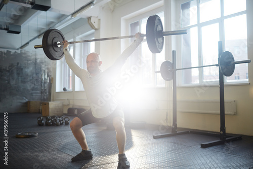 Sportsman squatting while lifting heavy barbell