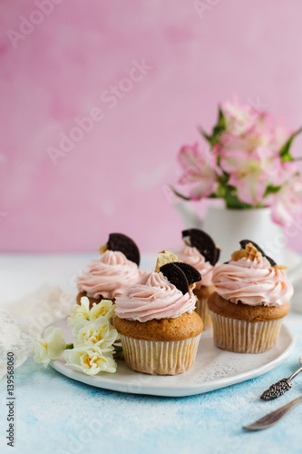 Vanilla cupcakes with chocolate chip cookies, decorated with flowers on a pink background