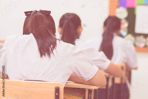 blurred of girl school students in uniform attending examination in a classroom in educational school: view of college people having exams in class on seat rows