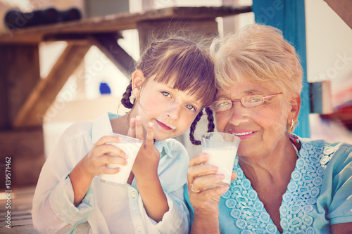 Grandmother with granddaughter drinking milk outdoors