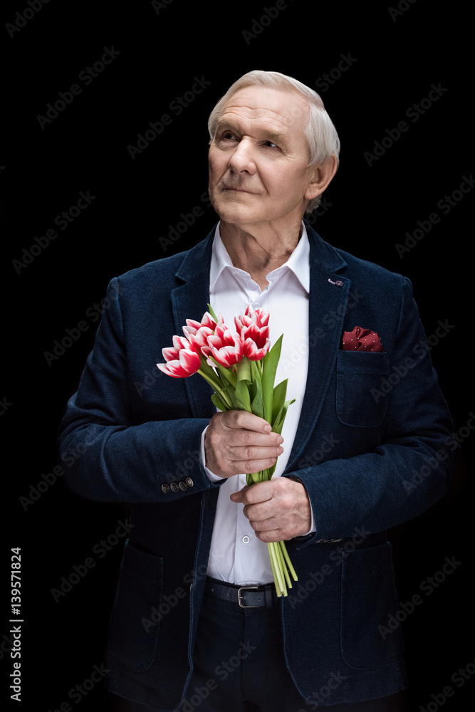 Pensive senior man holding tulips and looking away on black, spring holiday concept Pensive senior man holding tulips and looking away on black, spring holiday concept