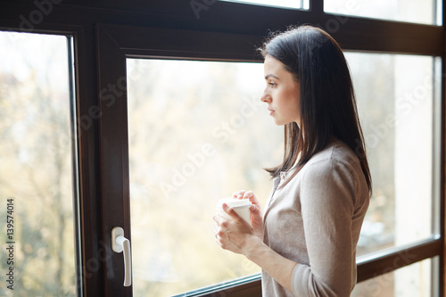 Girl with hot drink in plastic glass looking through window