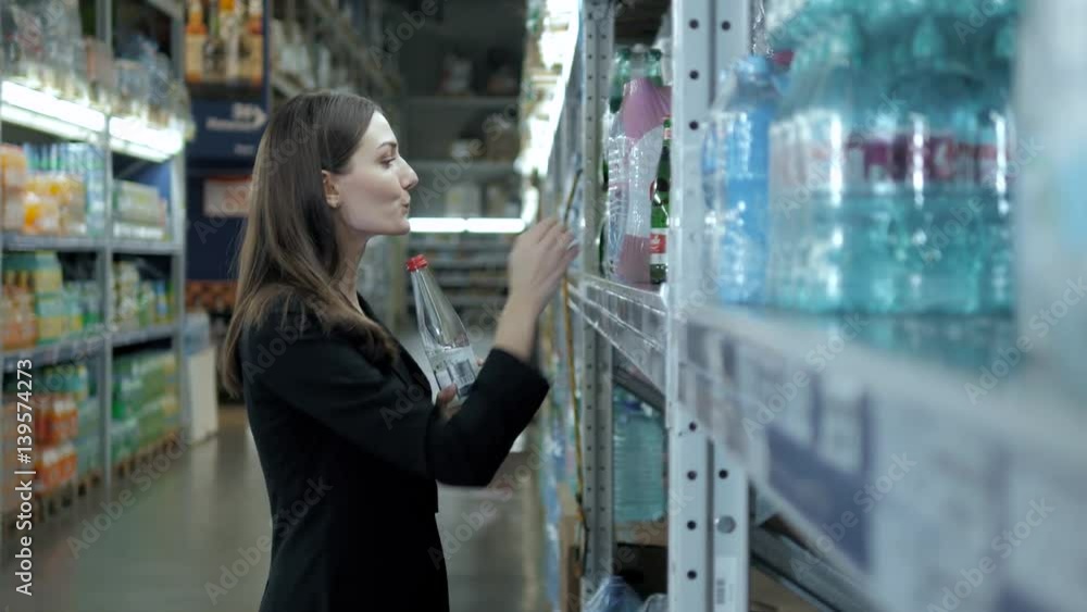 Smiling woman buying a bottle of water in grocery section of supermarket, businesswoman shopping Smiling woman buying a bottle of water in grocery section of supermarket, businesswoman shopping